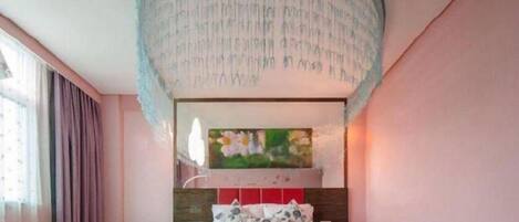 A bedroom with a bed, a painting above the bed, and a ceiling light fixture.