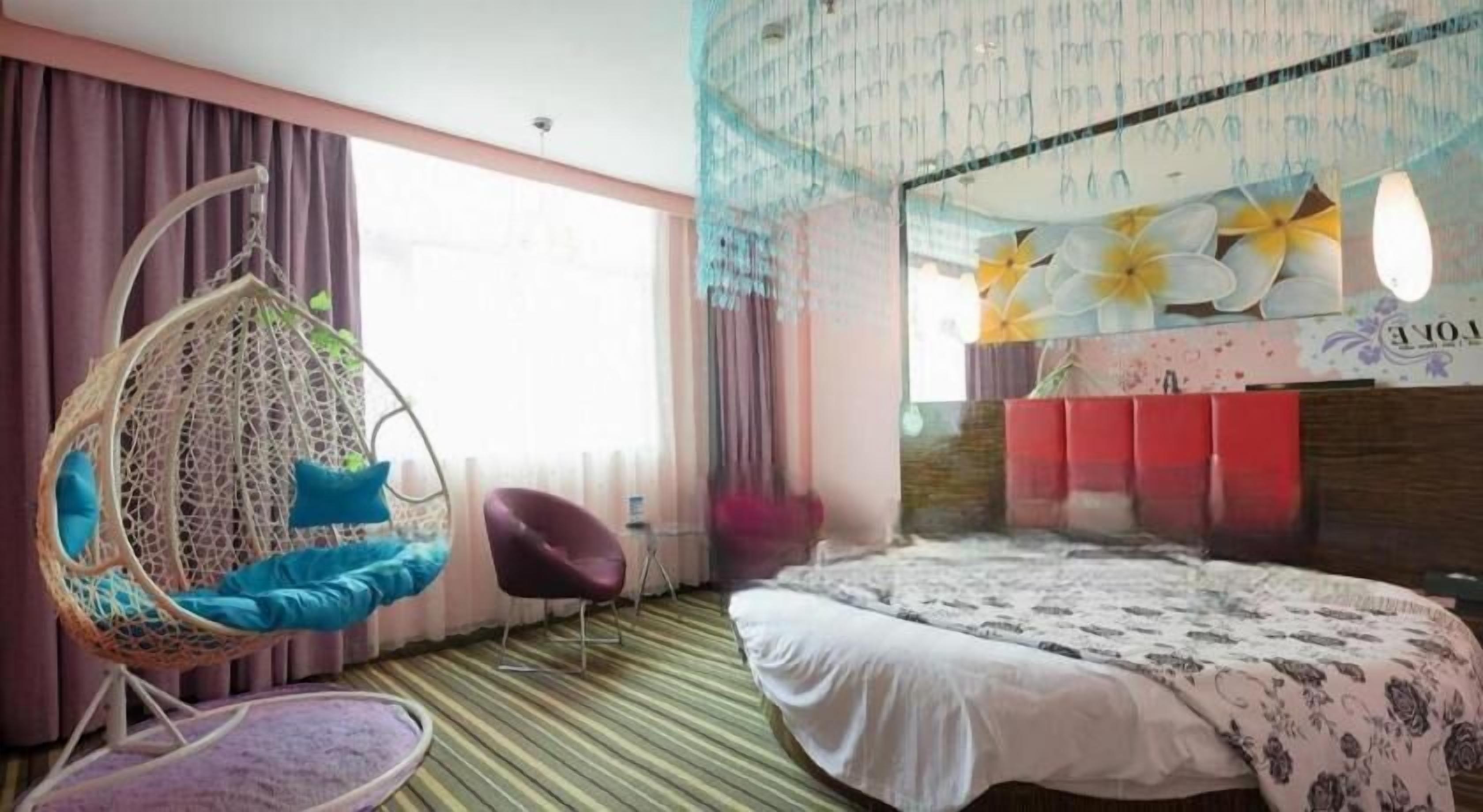 A bedroom with a hanging chair, a bed with a floral bedspread, and a view of the city through large windows.