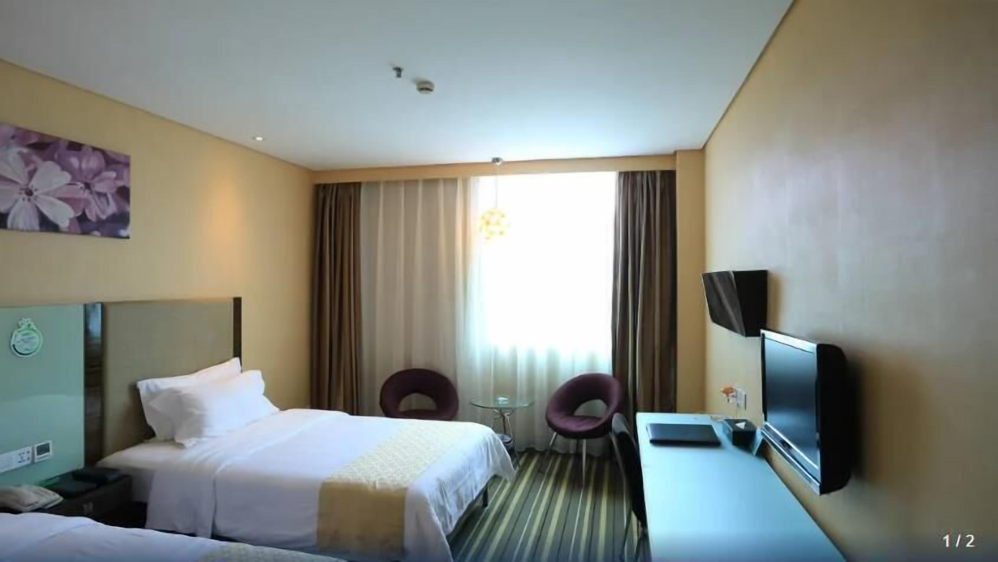 A hotel room with a bed, a desk, a chair, a TV, and a window with curtains.