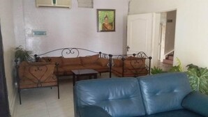 Un salon avec un ensemble de canapés marron, un canapé bleu et une petite table. Il y a une plante sur la gauche et une porte qui donne sur une autre pièce.