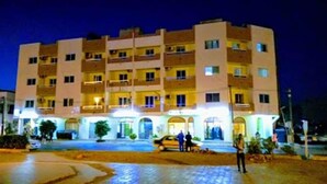 Un hôtel à plusieurs étages avec une cour intérieure, une voiture garée devant et une personne debout près de l’entrée.