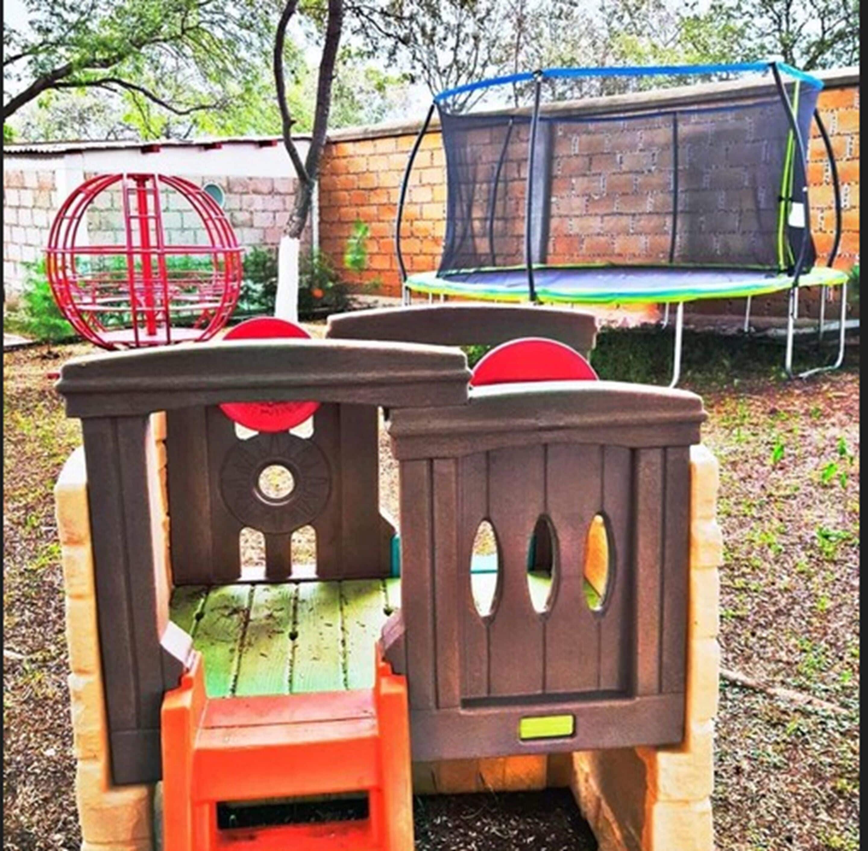 A wooden playhouse with a slide and a trampoline in the background.