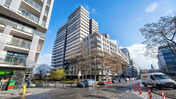 Un edificio de varios pisos con balcones, una calle empedrada y coches estacionados.