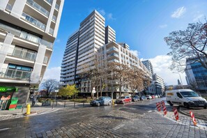 Un edificio de varios pisos con balcones, una calle empedrada y coches estacionados.