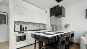 Una cocina moderna con armarios blancos, horno empotrado, cafetera y un comedor con mesa lista para dos.