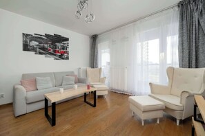 A modern living room with a sofa, armchairs, a coffee table, and a large window with sheer curtains. - Modern Apartment | Balcony | Parking | Downtown (Wrocław)