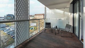 Un balcón con vista a coches estacionados y edificios, una silla, una mesa y un cartel con texto.