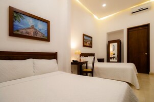 A hotel room with two beds, a desk with a lamp, a chair, a mirror, and two framed pictures on the wall.