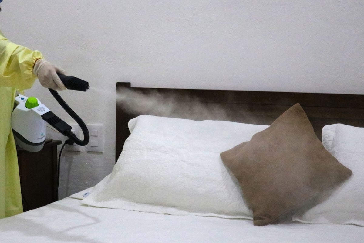 Una persona utilizando un limpiador a vapor en una cama con almohadas blancas y marrones.