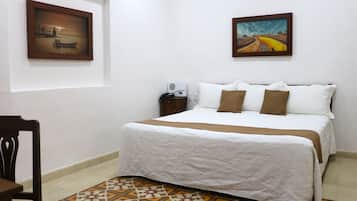 Una cama bien hecha con una colcha estampada, una silla y dos cuadros en la pared.