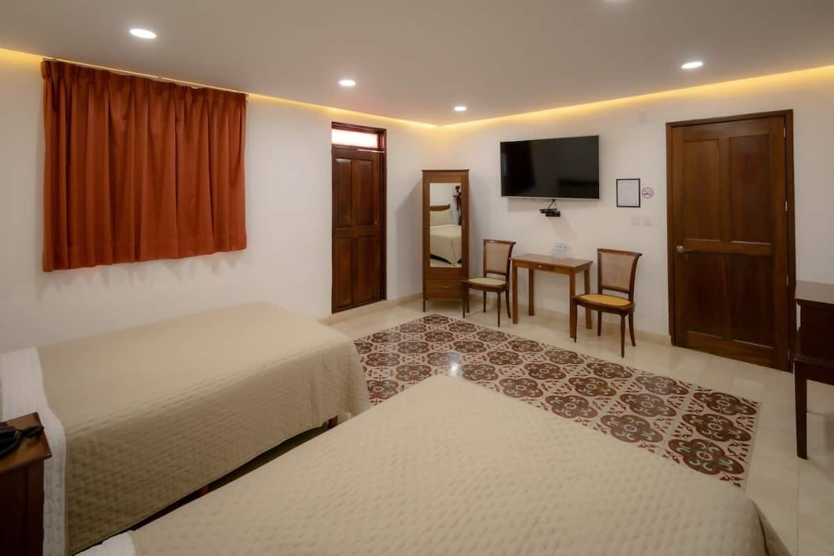 Un dormitorio con dos camas, televisor, escritorio con sillas y una alfombra estampada.