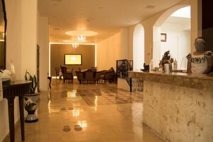 A hotel lobby with a reception desk, seating area, and a large screen.