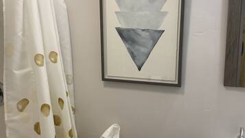 A bathroom with a toilet, a framed artwork above it, and a shower curtain with a pattern.