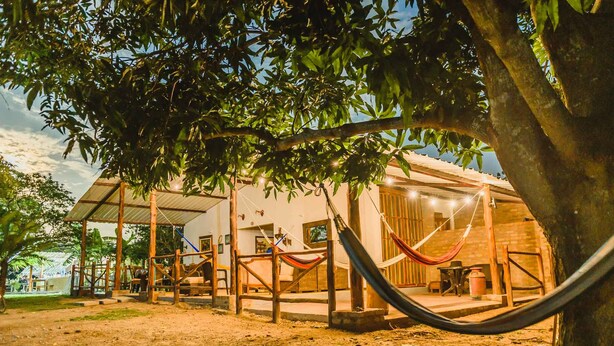 A rustic outdoor seating area with a hammock, wooden furniture, and a covered patio. - Reserva Natural El Encanto de Guanapalo (San Luis de Palenque)