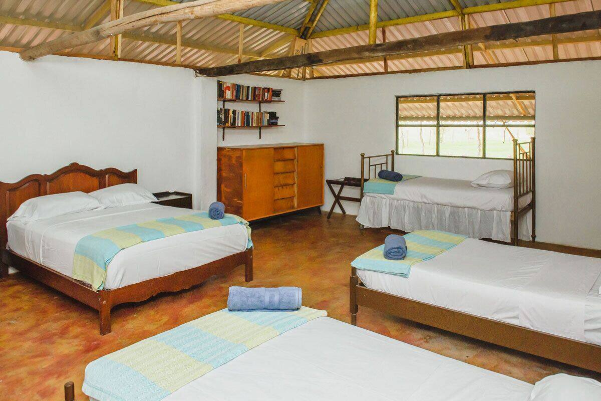Una habitación con tres camas de madera, un armario de madera, una mesita pequeña y una estantería.