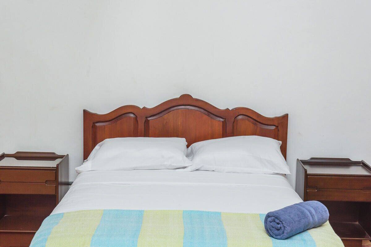 Una cama con cabecera de madera, almohadas blancas y una manta a rayas.