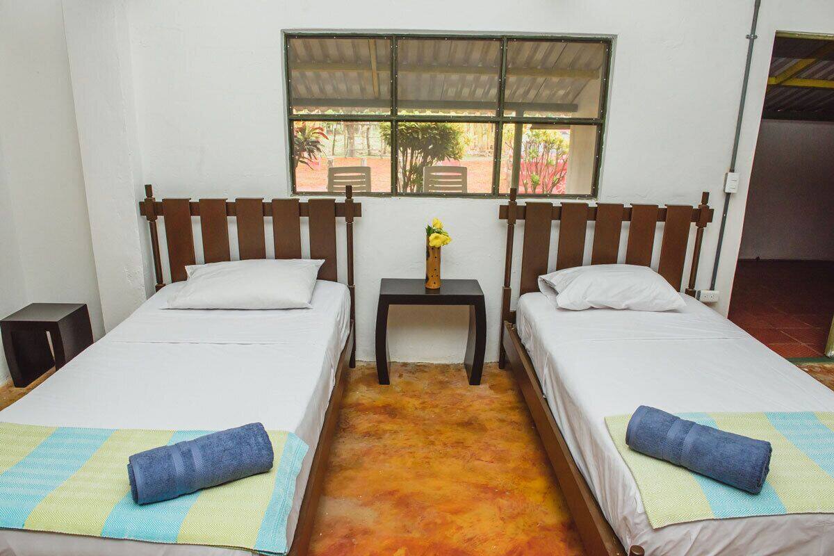 Una habitación con dos camas, una mesita y una ventana.