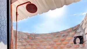 A brick-walled shower area with a curved roof, a showerhead, and a pair of black shoes hanging on the wall. - Reserva Natural El Encanto de Guanapalo (San Luis de Palenque)