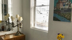 A room with a wooden dresser, a mirror, a window with blinds, a painting on the wall, and a vase with flowers. - Minutes to Midtown NYC, sunny, super clean modern 2 bedroom beautiful apartment (West New York)