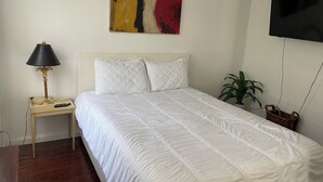 A bedroom with a bed, a nightstand, a lamp, a painting, a television, and a potted plant. - Minutes to Midtown NYC, sunny, super clean modern 2 bedroom beautiful apartment (West New York)