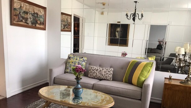 A living room with a grey sofa, patterned cushions, a glass coffee table with a blue vase, a patterned rug, and a chandelier. - Minutes to Midtown NYC, sunny, super clean modern 2 bedroom beautiful apartment (West New York)
