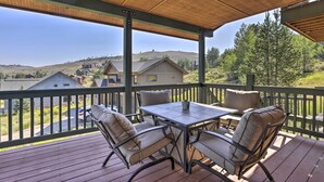 Une terrasse extérieure couverte, dotée d’une table et de chaises, qui offre une vue sur un quartier résidentiel avec ses maisons et ses collines.