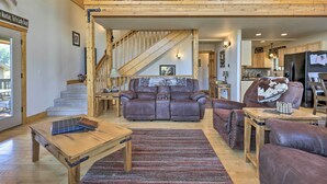 Un salon spacieux avec un canapé en cuir marron, une table basse en bois et un escalier menant à l’étage supérieur.