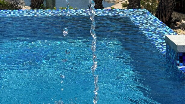 Ein Schwimmbad mit klarem, blauem Wasser, umgeben von Palmen und einer Zierbrunnen.