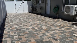 Een terras met een vloer van patroon tegels, een wit hek en een gebouw met een airconditioning.