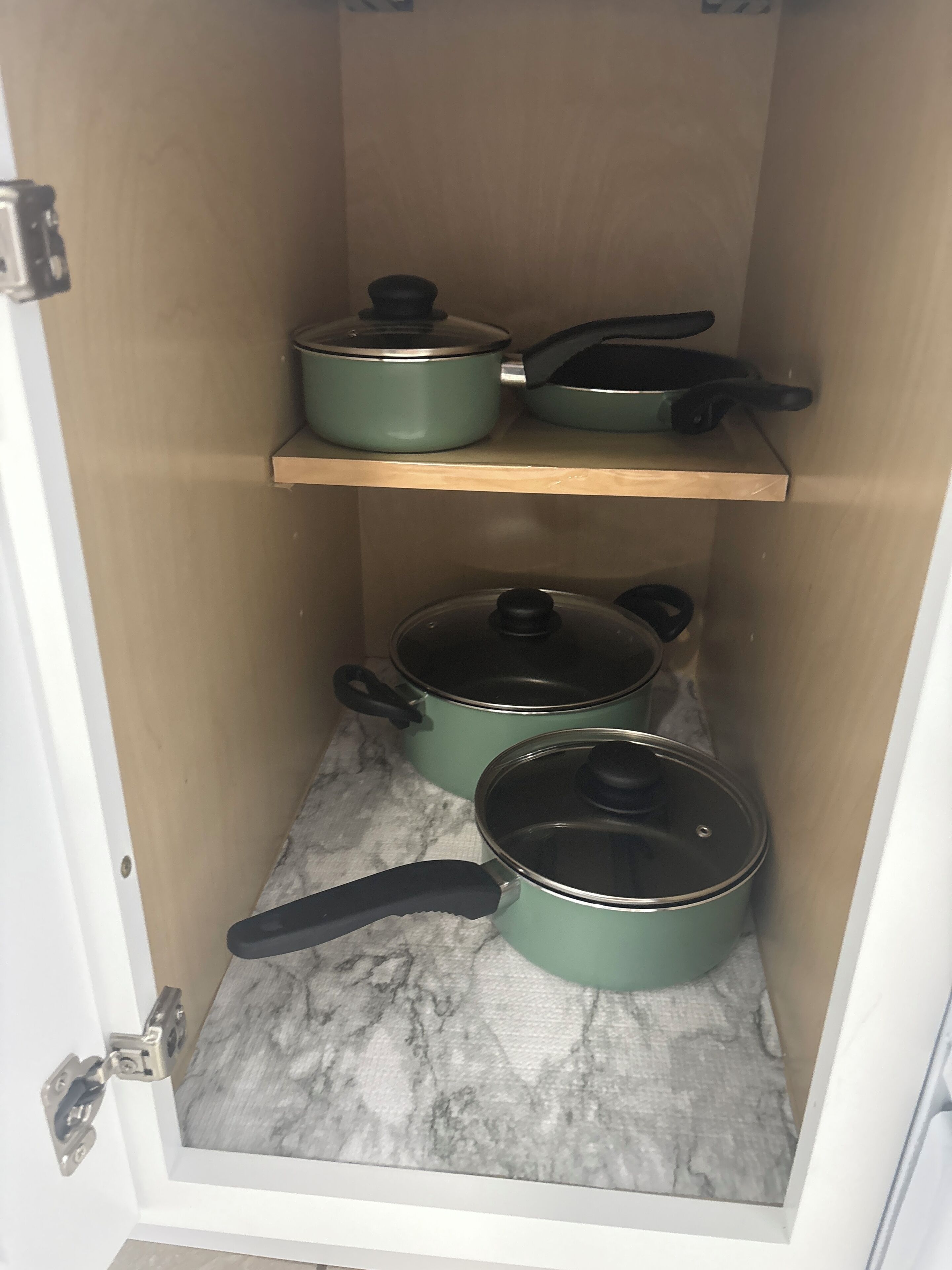 A kitchen cabinet with two shelves, each holding pots and pans.