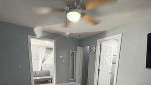 Een slaapkamer met een bed, een plafondventilator en een deur naar een andere kamer.