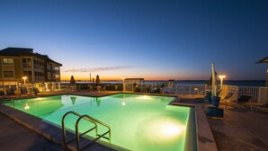 Ein Schwimmbecken mit Sonnenuntergangsblick, Liegestühle und ein mehrstöckiges Gebäude.