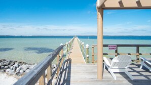 Eine Holzstele führt zu einem Strand, wo ein Schild 'No Diving Allowed' zu sehen ist, zusammen mit weißen Stühlen und einem klaren Blick auf den Ozean.