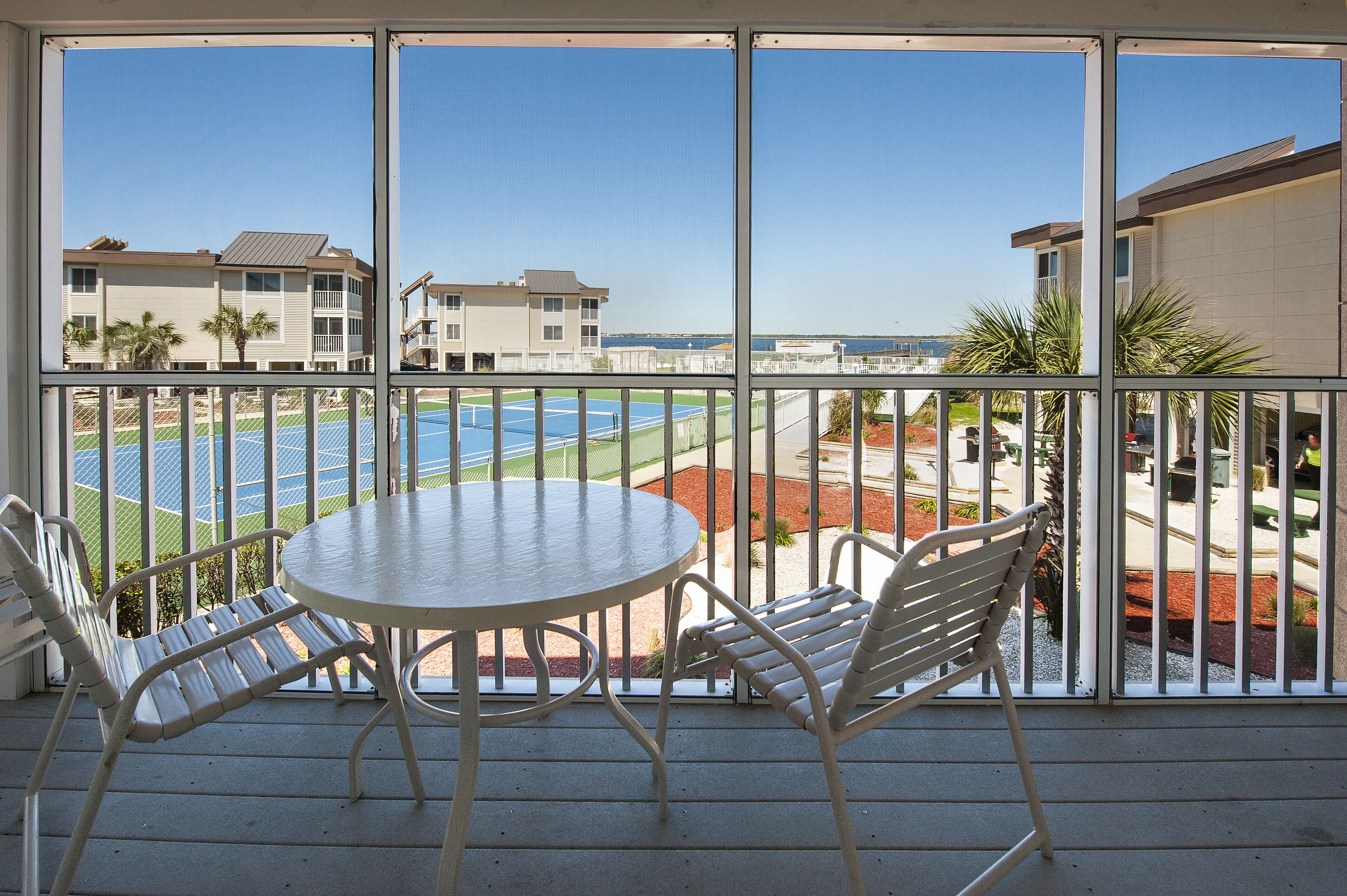 A balcony with a table and chairs, overlooking a tennis court and buildings.