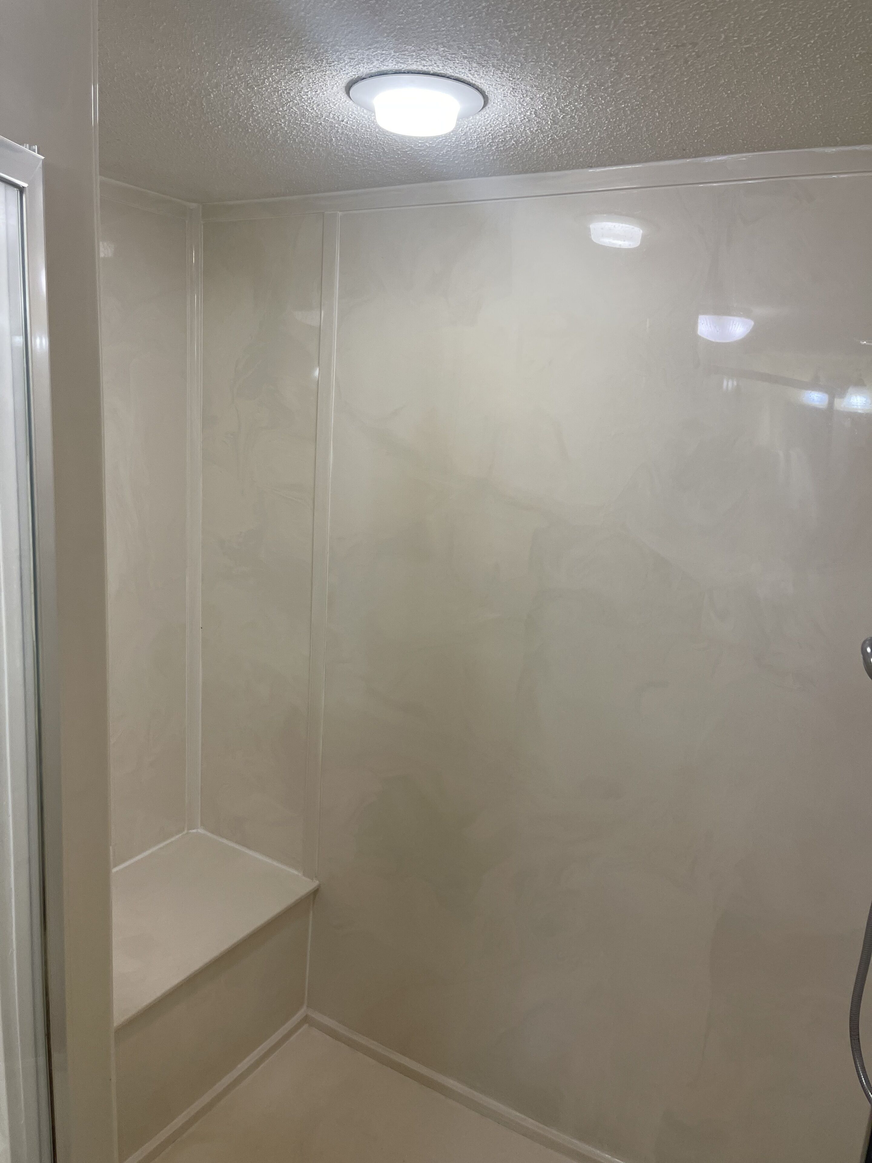 Een badkamer met een douche, een bankje en een plafondlamp.