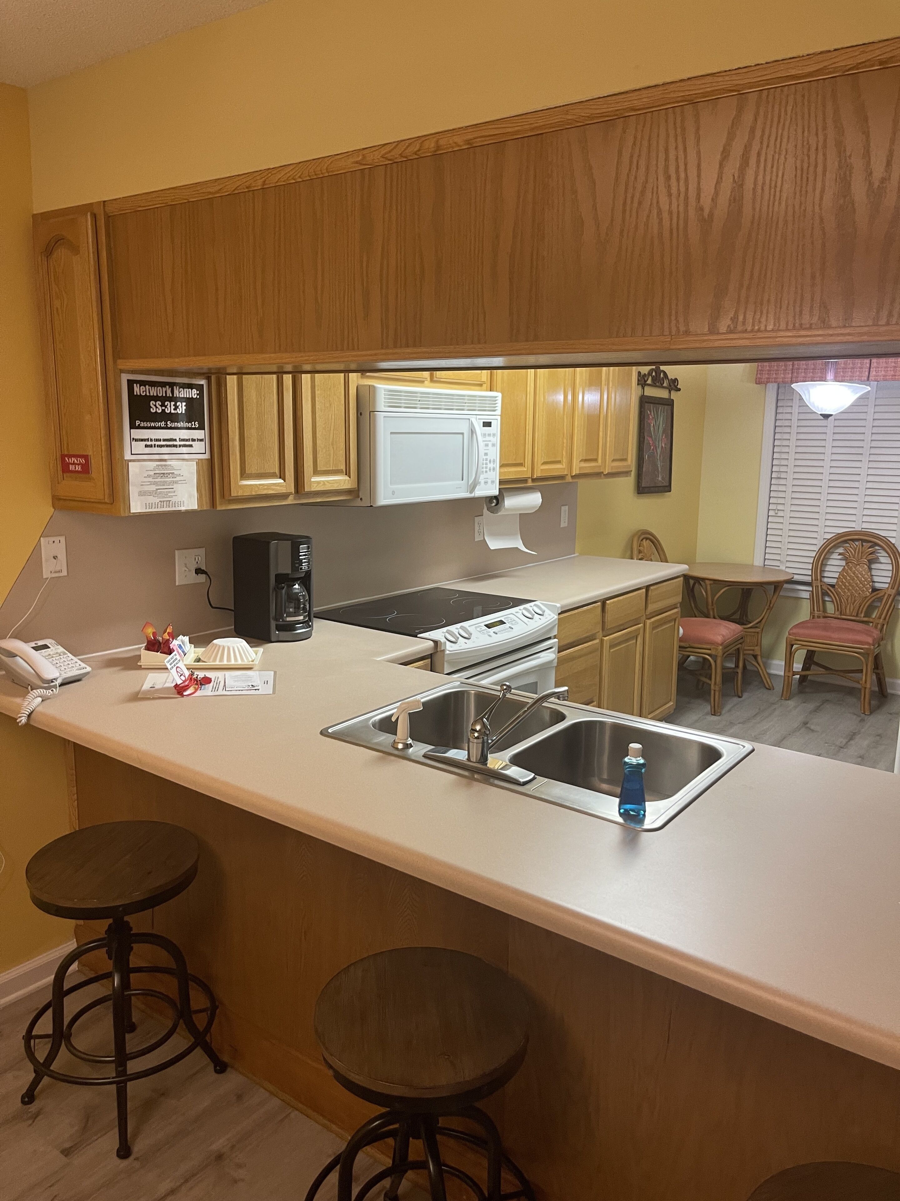 A kitchen with wooden cabinets, a microwave, a stove, a sink, and a bar stool.