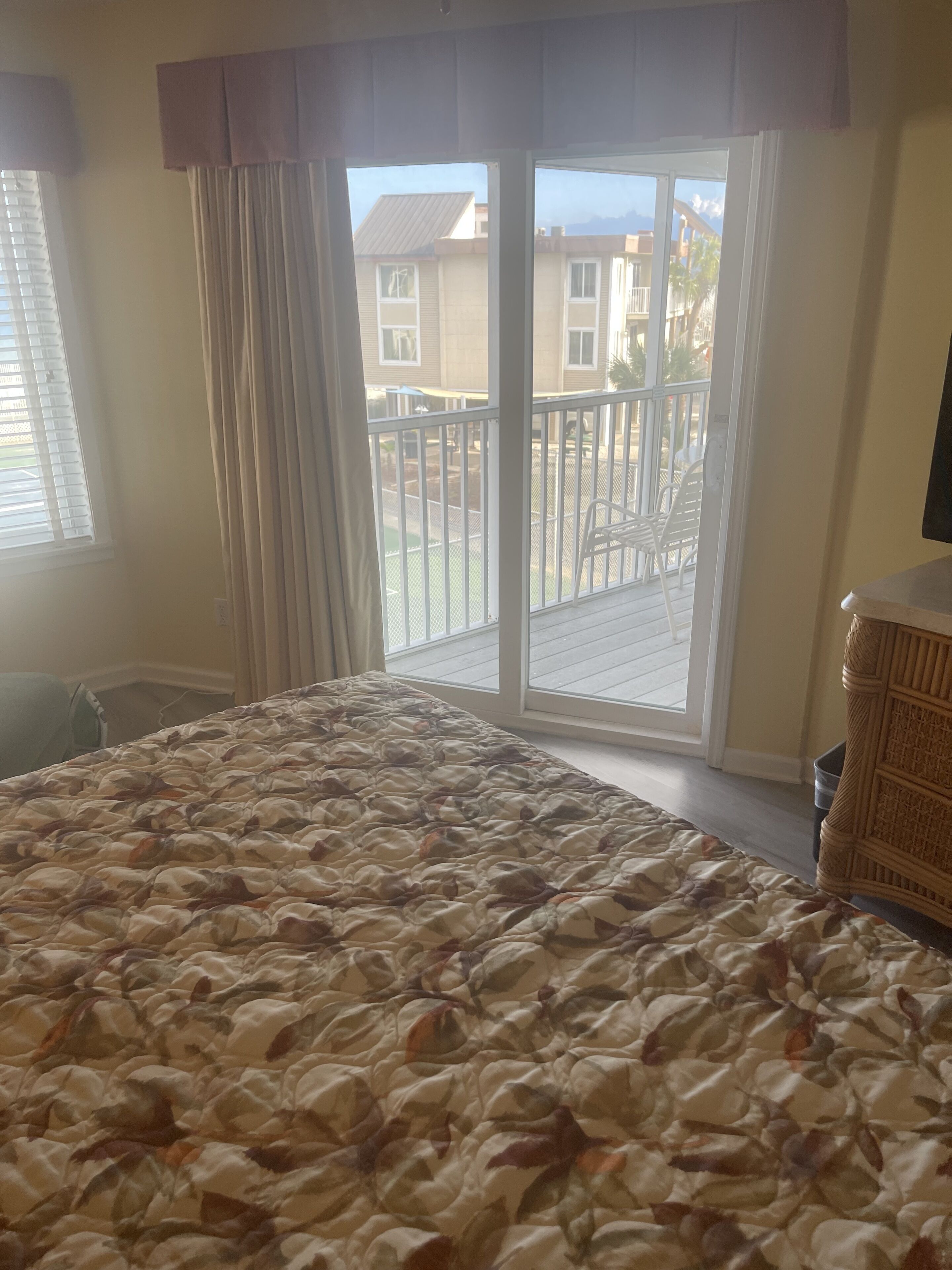 A bedroom with a large bed, a sliding glass door to a balcony, and a view of buildings and a mountain.