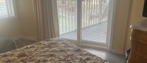 A bedroom with a large bed, a sliding glass door to a balcony, and a view of buildings and a mountain.