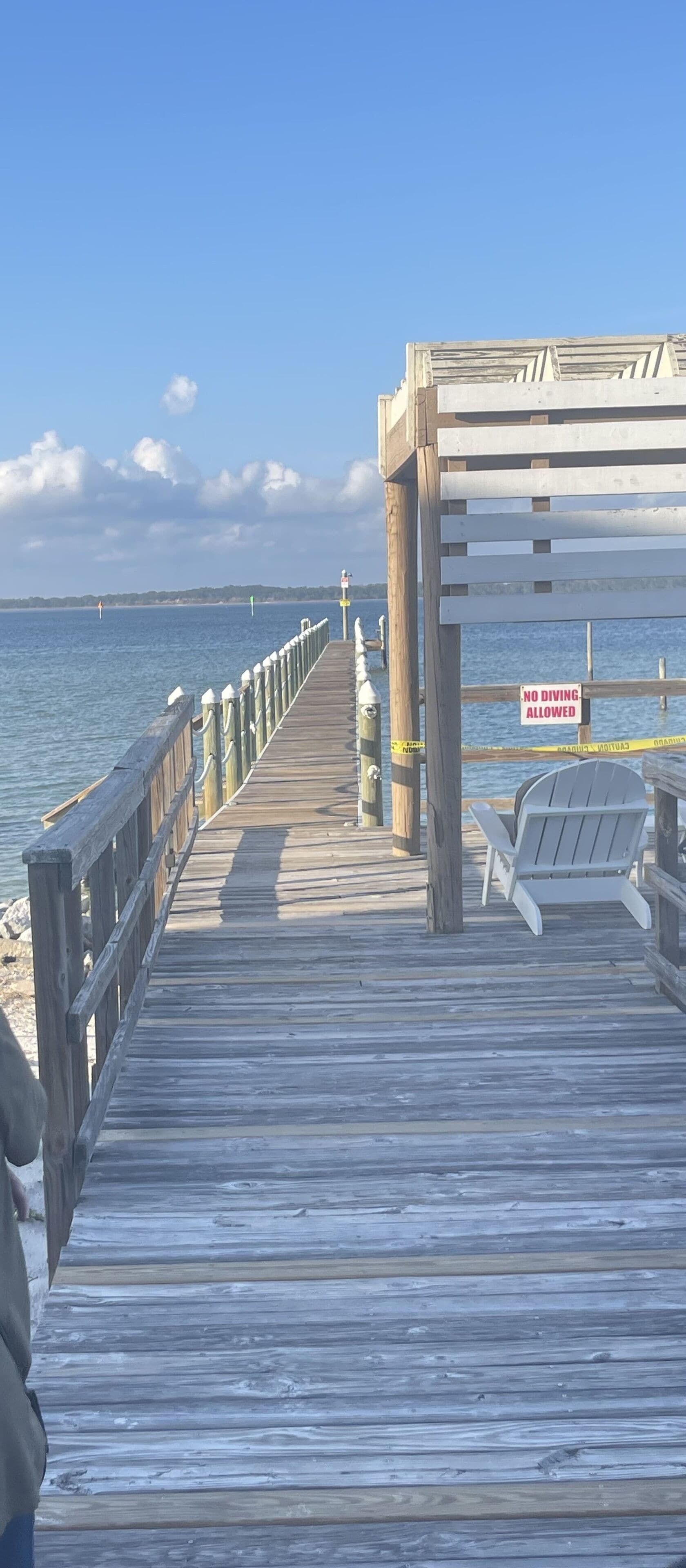 A wooden pier extending into the water with a 'No Diving Allowed' sign, a lifebuoy, and a chair.