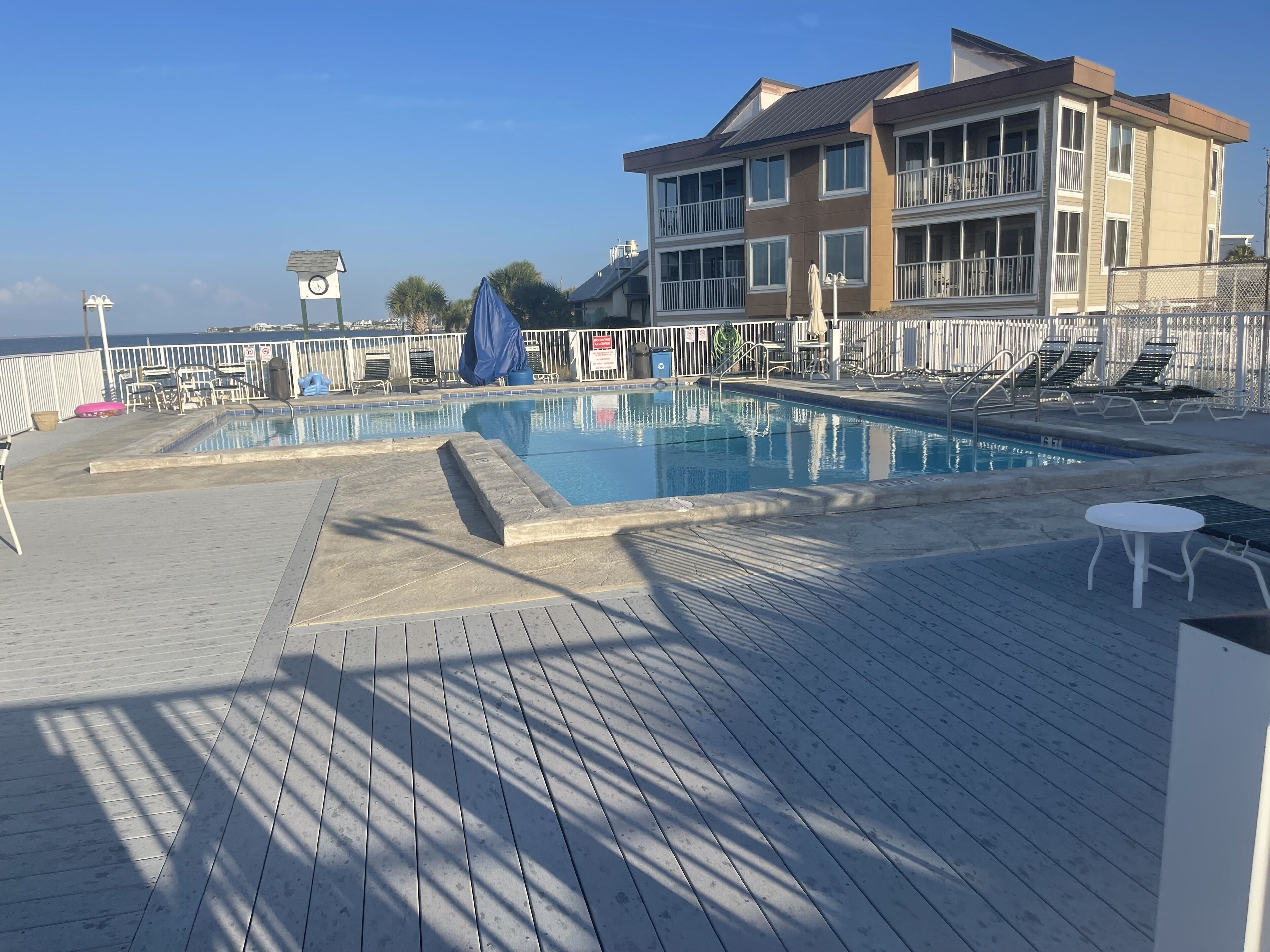 Ein Poolbereich mit Holzterrasse, Liegestühlen und einem Gebäude mit Balkonen.
