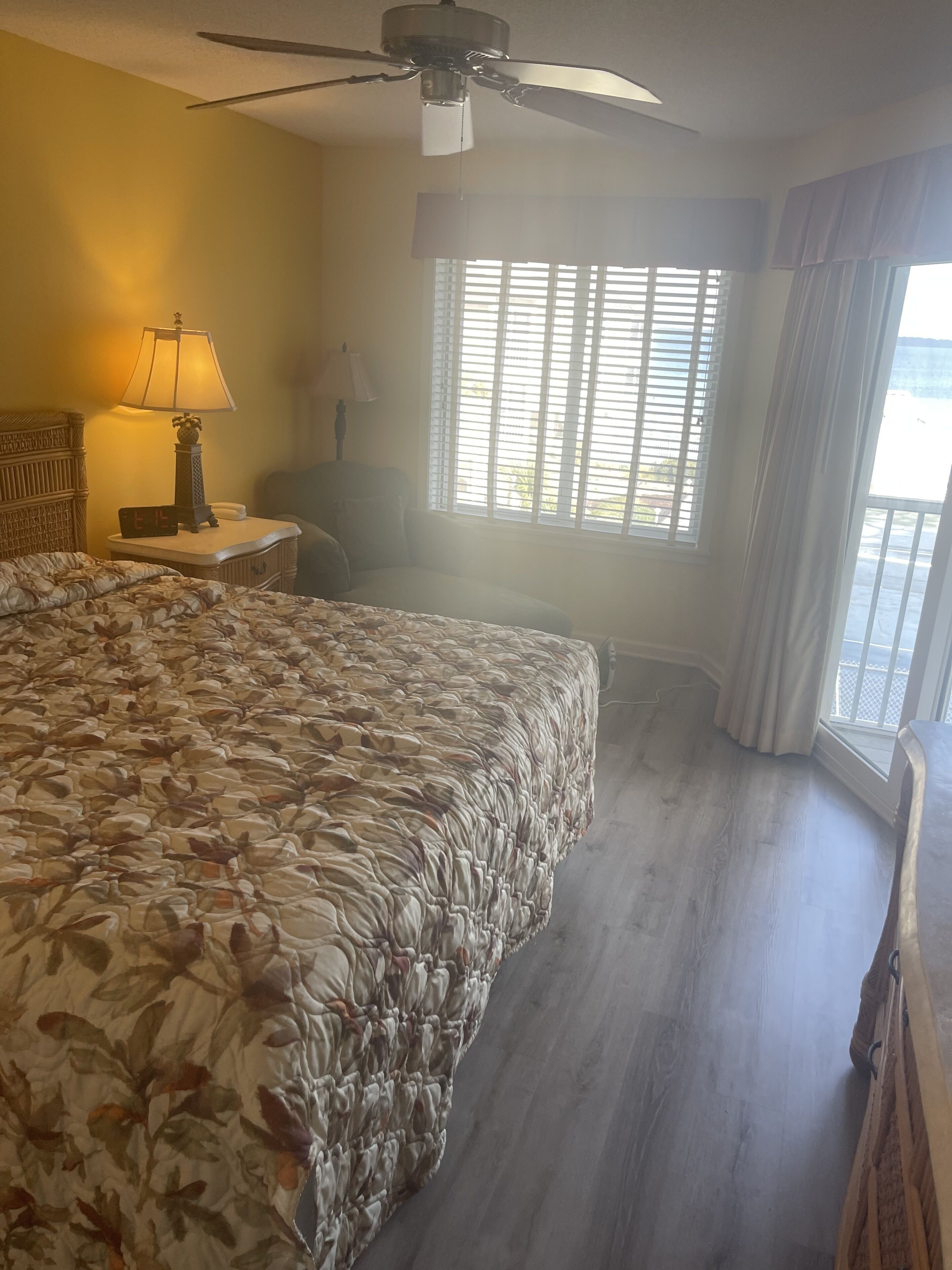 Une chambre d’hôtel avec un grand lit, un ventilateur de plafond, une fenêtre avec des stores et une vue sur l’extérieur.