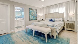 A bedroom with a bed, bench, ceiling fan, and artwork.