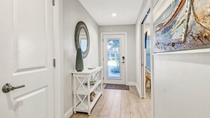 A hallway with a white door, a console table with a mirror, and a painting on the wall.
