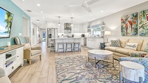 A modern kitchen with white cabinets, a central island with bar stools, and a ceiling fan.