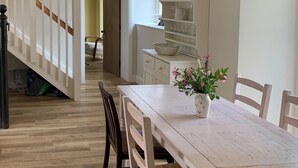 A dining area with a wooden table, chairs, and a vase of flowers. A staircase is visible in the background leading to another room. - The Stable was renovated in 2020 to enhance your stay in the Canterbury area. (Womenswold, near Canterbury)