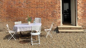 A table set outdoors with a brick wall backdrop, a white chair, and a small table with a vase of flowers. - The Stable was renovated in 2020 to enhance your stay in the Canterbury area. (Womenswold, near Canterbury)