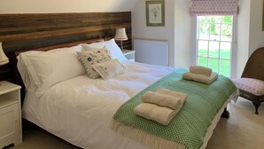 A neatly made bed with white linens and decorative pillows, a green checkered throw blanket, and two rolled towels. - The Stable was renovated in 2020 to enhance your stay in the Canterbury area. (Womenswold, near Canterbury)