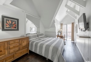 Een slaapkamer met een schuine wand, een bed met gestreepte beddengoed, een houten dressoir en een ingelijst beeld op de muur.