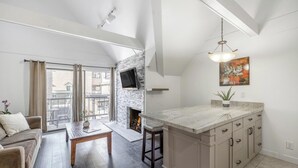A modern kitchen with a stone fireplace, a large island with drawers, and a dining area with a table and chairs. - Ski-In/Ski-Out Park City Mountain Resort 1BR+Loft Sleeps 6-A/C & Fireplace (Park City)