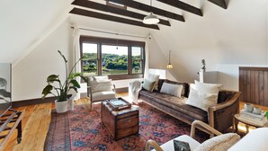 A cozy loft-style living room with a large window, wooden beams, a patterned rug, and a comfortable seating area. - The Pearl, NH hidden luxury close to the Quinnipiac River in historic property (New Haven)